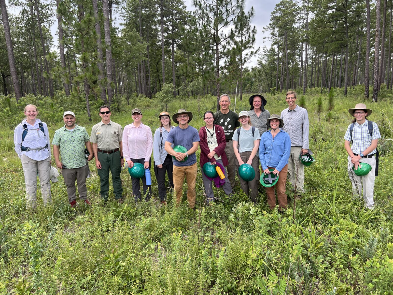 A photo of a group of people smiling in front of a forested area.