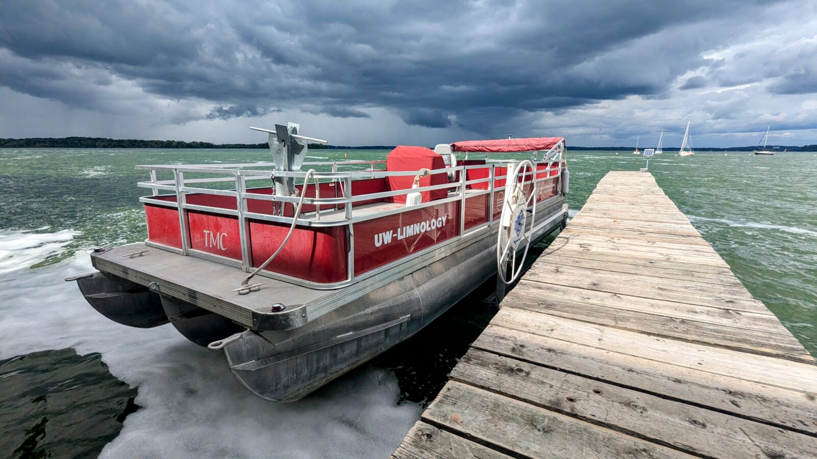 A photo of a red pontoon boat at a dock with a storm looming over the lake behind it.