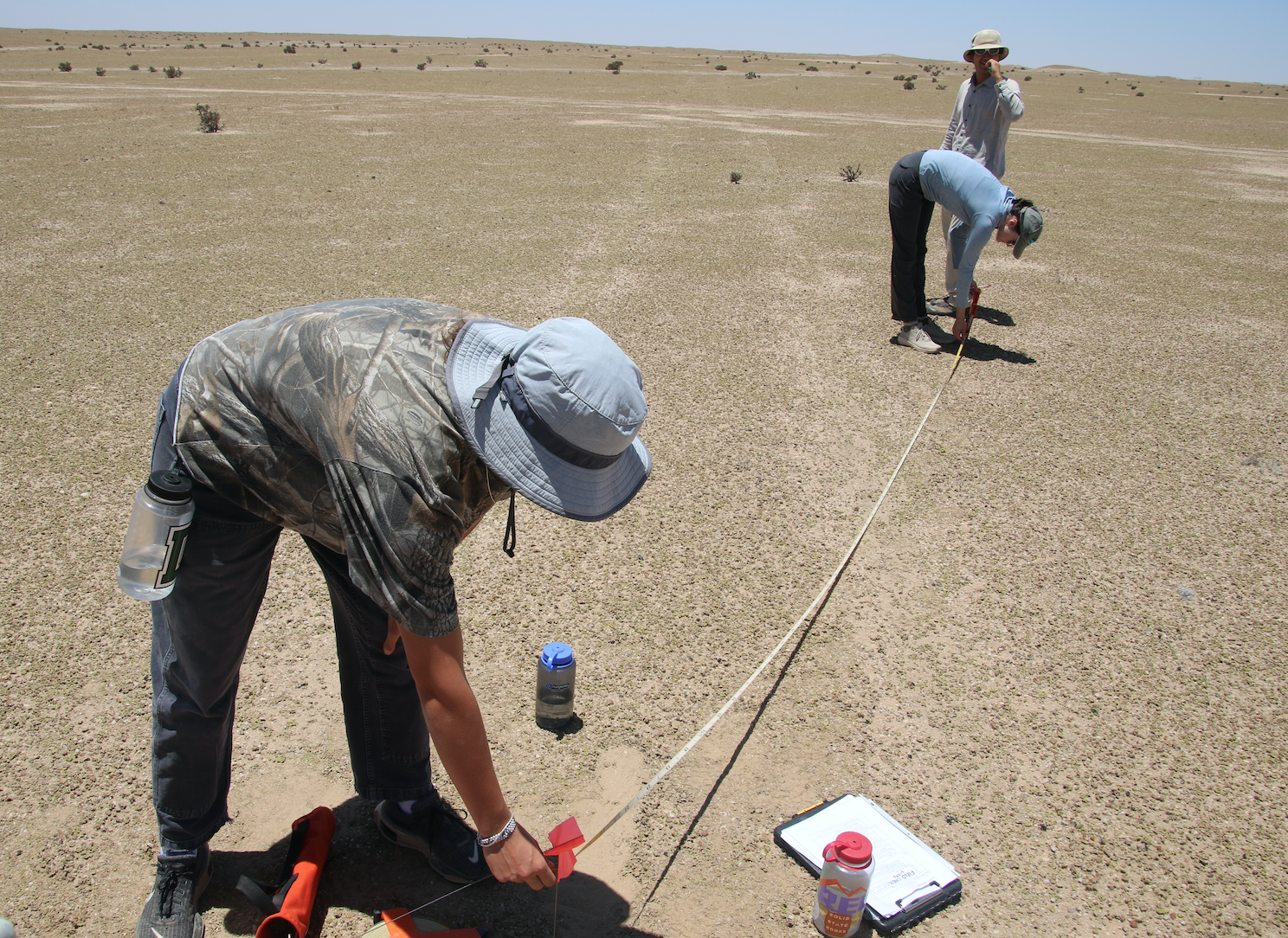 People take measurements in a dry field site.