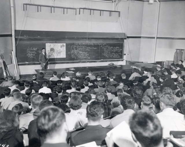 A historic image of an instructor teaching an auditorium full of students.