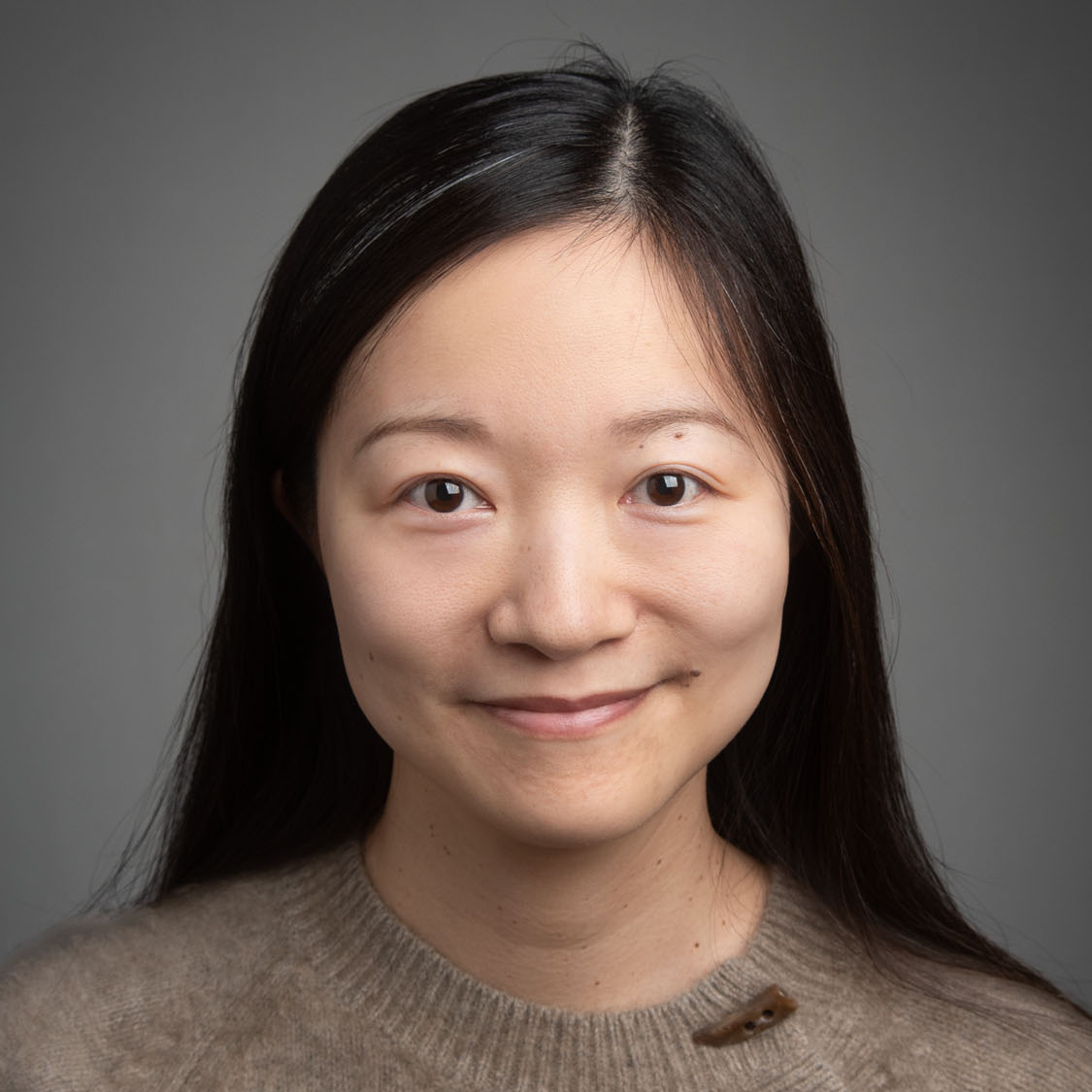 a portrait of Professor Shan He in front of a grey studio background
