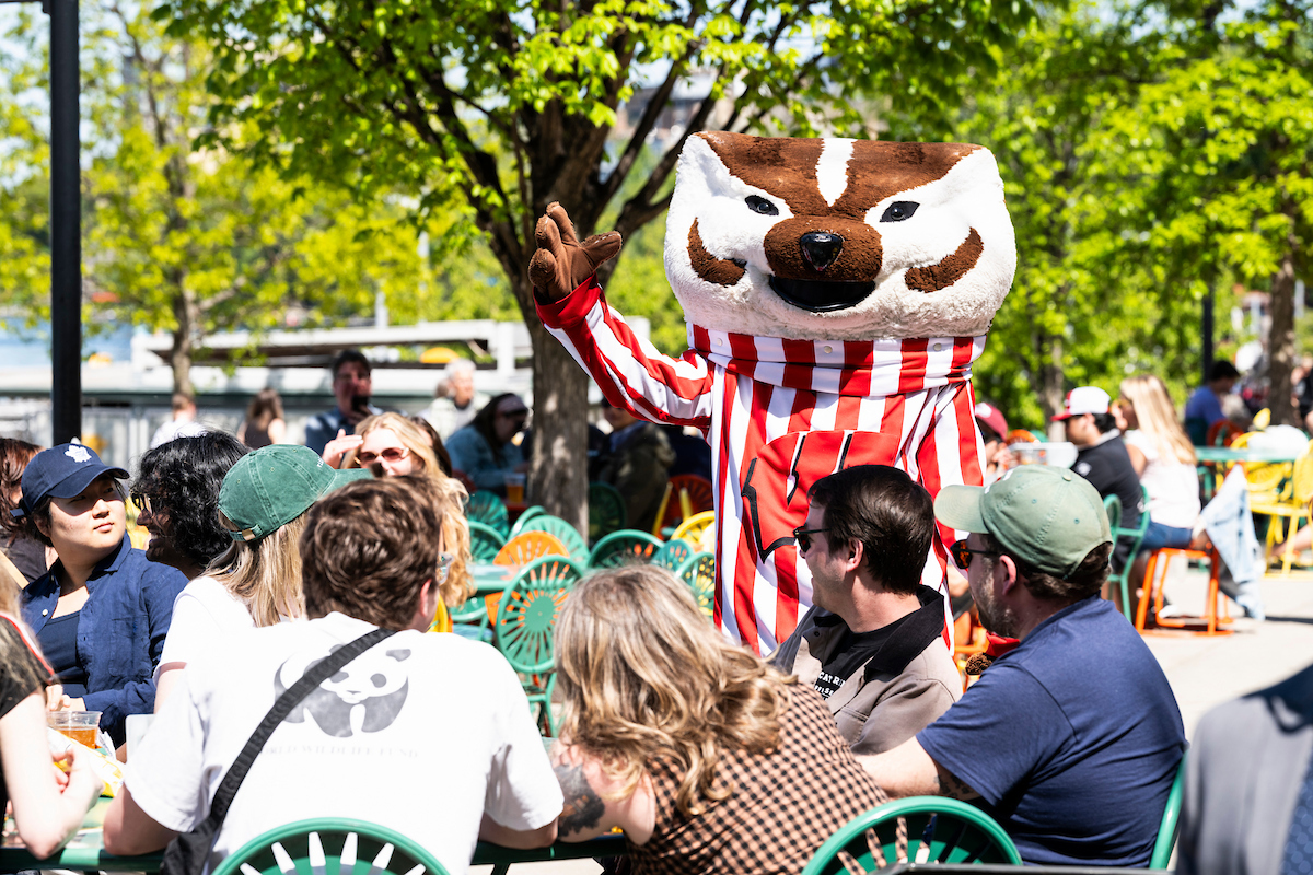 Bucky Badger, the mascot of UW–Madison waves over a crow of folks seated at the Memorial Union Terrace.