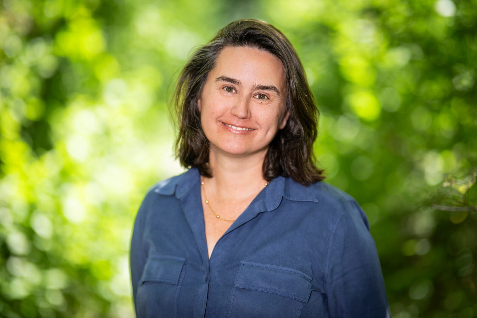 A portrait of a person smiling with greenery behind them.